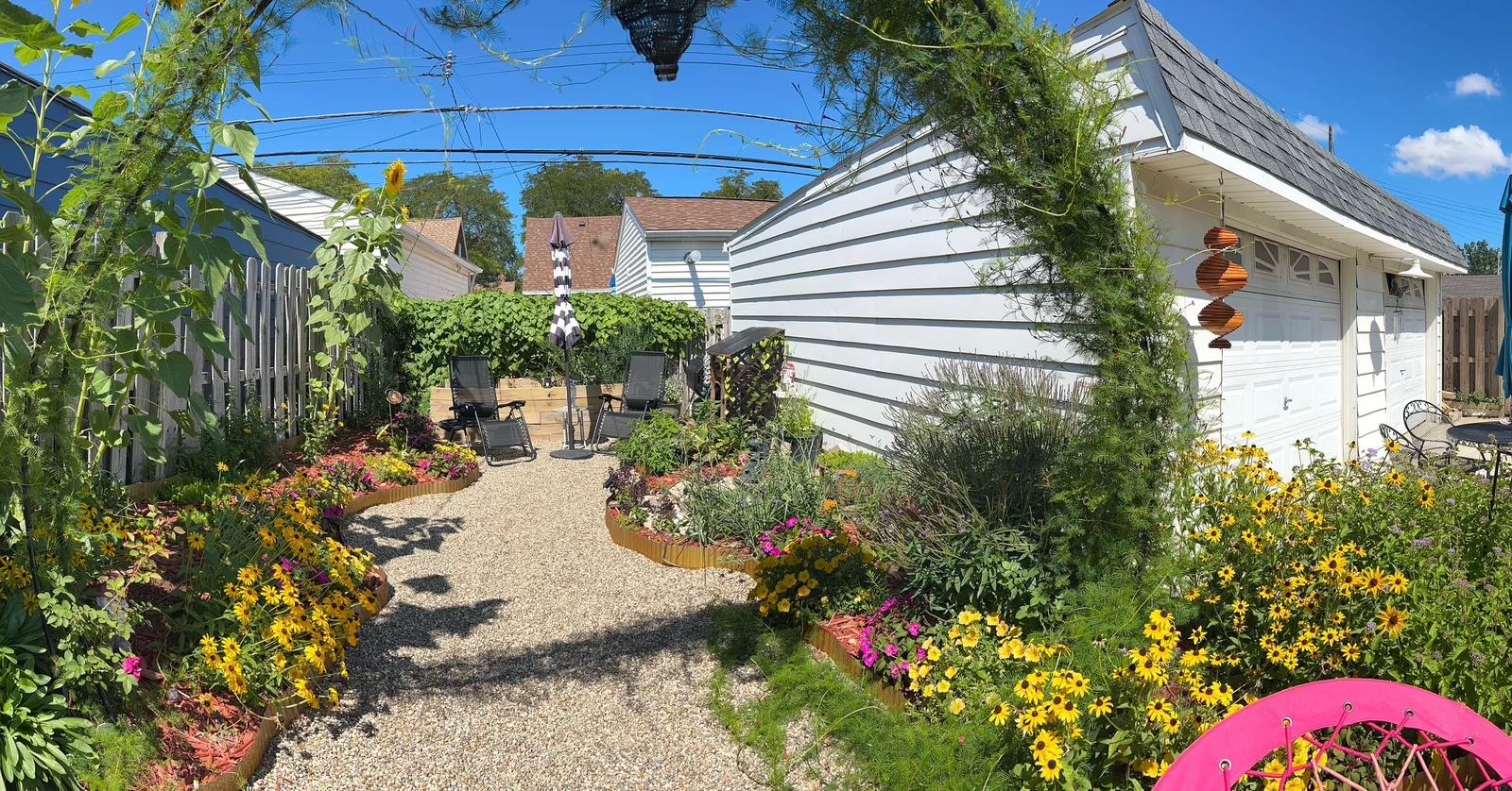 Wide gravel garden path bordered by native plants, yellow flowers, and a peaceful seating area